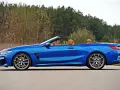 Niebieski roadster z brązową skórzaną tapicerką, zaparkowany na drodze z widokiem na las.