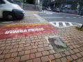 Czerwony pas na chodniku z napisem "UWAGA POJAZDY" informuje o przejściu sugerowanym. W tle widać samochody i schody.