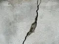 Pękające ściany w nowym domu, widoczna głęboka szczelina w jasnoszarym tynku, odsłaniająca fragmenty betonu.