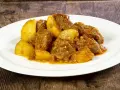 Un saporito spezzatino di vitello con patate, servito su un piatto bianco, su uno sfondo di legno scuro.