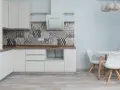 Cocina moderna con armarios blancos, salpicadero geométrico y suelo gris claro. Mesa redonda con sillas blancas.