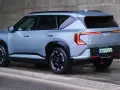 Nowoczesne kia ev5 w kolorze jasnoszarym, z charakterystycznymi tylnymi światłami, zaparkowane przy betonowej ścianie.