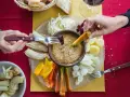 Un gruppo di mani intinge verdure nella bagna cauda, un piatto conviviale.