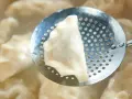 Pieróg wyjmowany łyżką cedzakową z gotującej się wody.