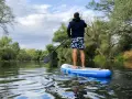 Mann auf SUP-Tour auf einem ruhigen Fluss, umgeben von üppiger Vegetation.