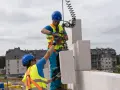 Dwóch budowlańców w kaskach i kamizelkach odblaskowych montuje bloczki z betonu komórkowego. Praca idzie w **silka tempo**, bo budowa postępuje.