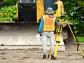 Geodeta w kamizelce odblaskowej z niwelatorem i dokumentami. Zastanawiasz się, ile zarabia geodeta?