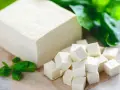 Kostka tofu, z czego jest zrobione, pokrojona w kostkę i ozdobiona listkami bazylii.