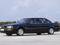 Ciemnoniebieski Audi V8 z lat 90. stoi na pustej drodze, z drzewami w tle.