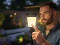Un homme touche une lampe solaire extérieure, illustrant le fonctionnement on/off de l'éclairage de jardin.