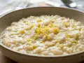 Un cremoso risotto al limone, guarnito con scorza di limone e scaglie di parmigiano, pronto per essere gustato.