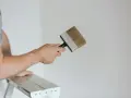 Person på en stege håller en bred pensel redo att måla huset vitt.