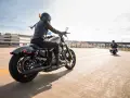 Kobieta w skórzanej kurtce i kasku jedzie na stylowym motocyklu dla kobiety. Wiatr rozwiewa jej włosy, a słońce odbija się od chromowanych elementów.