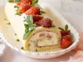 Eine köstliche Erdbeer Biskuitrolle, verziert mit frischen Erdbeeren, Minze und Pistazien, auf einem weißen Teller.