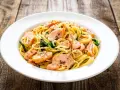 Makaron spaghetti z łososiem i szpinakiem na białym talerzu, na drewnianym tle.
