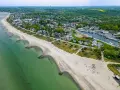 Luftaufnahme eines Strandes mit grüner Ostsee, Häusern und einem Yachthafen. Ein idyllischer Ort für ruhige Orte an der Ostsee.