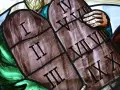 Witraż przedstawia kamienne tablice z wyrytymi cyframi rzymskimi, symbolizujące dekalog przykazania. Widoczne są cyfry I, II, III, IV, V, VI, VII, VIII, IX, X.