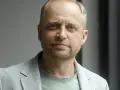 Piotr Adamczyk, znany z wielu filmów, seriali i programów, w jasnej marynarce i zielonej koszulce.