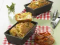 Cake tomates séchées feta, un délice salé aux herbes fraîches. Une tranche est posée sur un cake encore dans son moule.