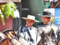 Deux huasos rient joyeusement à cheval, vêtus de ponchos traditionnels et de chapeaux.