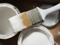 Pędzel z białą farbą nad otwartymi puszkami. Idealne rozwiązanie, czym uzupełnić ubytki w elewacji.