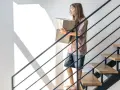 Młoda dziewczyna z pudełkami wchodzi po nowoczesnych schodach. Jakie schody do domu? Te z drewnianymi stopniami i metalową balustradą.