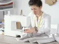 Krawcowa skupiona na pracy przy maszynie, dobiera odpowiednie rozmiary igieł do tkaniny.