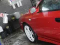 Ręka trzyma opryskiwacz, rozpylając pianę na czerwony samochód.