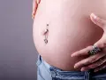 Brzuszek w ciąży z ozdobnym kolczykiem w pępku. Warto pamiętać, że kolczyk w pępku w ciąży może być problematyczny.