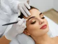 Une esthéticienne crée des sourcils brossés vers le haut sur une cliente, perfectionnant son regard avec précision.