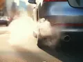 Samochód kopci na biało z rury wydechowej, tworząc gęstą chmurę pary wodnej.