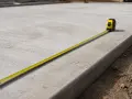 Mètre ruban sur une dalle de béton fraîchement coulée, 15 cm d'épaisseur. Le temps de séchage est crucial.