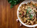 Pyszne danie z makaronem malfadine czy tagliatelle z grzybami i parmezanem, podane na drewnianym blacie.