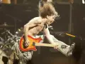 Un guitariste en plein saut, cheveux au vent, déchaîne sa guitare. Un vrai héros de la guitare en pleine action.