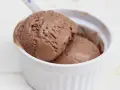 Dos bolas de cremoso helado de chocolate derritiéndose en un cuenco blanco.