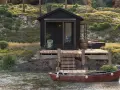 Svart stuga vid vattnet med altan och båt. Kanske behövs bygglov altan för denna idylliska plats.