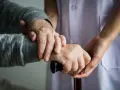 Manos de un anciano y un cuidador sujetando un bastón. Apoyo y cuidado para la dependencia.