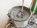 Secchio con malta fresca in preparazione, mostrando la differenza tra malta e cemento. Un sacco di cemento è visibile sullo sfondo.