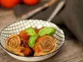 Zwei herzhafte involtini originalrezept in Tomatensoße, garniert mit Basilikum, in einer Schale auf Holztisch.