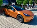 Pomarańczowa Tesla na tle ładowarek Supercharger.