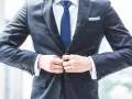 Mężczyzna zapina **za ciasną marynarkę**. Widać białą koszulę, granatowy krawat i niebieską poszetkę.