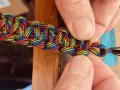 Mani che chiudono un braccialetto colorato con filo, mostrando come chiudere un braccialetto con filo.
