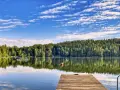 Holzsteg am ruhigen Badesee Dresden, umgeben von üppigem Grün und blauem Himmel mit Wolken.