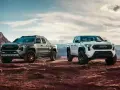 Dwa nowe modele toyota pickup, biały i szary, gotowe na przygodę w surowym, pustynnym krajobrazie.