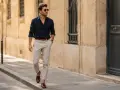 Mężczyzna w granatowej koszuli i beżowych spodniach, prezentujący styl smart casual, spaceruje ulicą.