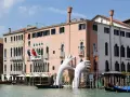 Enorme installazione di mani bianche emerge dal Canal Grande, davanti al museo arte contemporanea Venezia. Gondole ormeggiate.