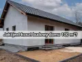 Szary dom w trakcie budowy, z widocznym dachem i oknami. Na froncie napis "Jaki jest koszt budowy domu 100 m²?".