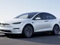 Biały Tesla X w ruchu, kierowca w okularach. Zastanawiasz się nad jego ceną?