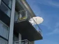 Balcon en béton moderne, prêt pour une rénovation. Des plantes en pot et un parasol blanc attendent le soleil.