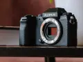 Czarny aparat Fujifilm X-S20 z obiektywem bez obiektywu, leżący na drewnianym stole obok książki.